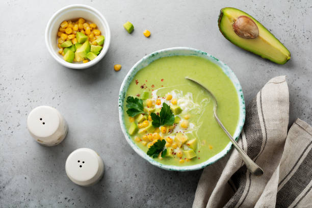 istock Homemade tender soup puree from avocado and corn with cream in rustic ceramic plate on gray concrete old background. Selective focus. Top view. Copy space. 984972542