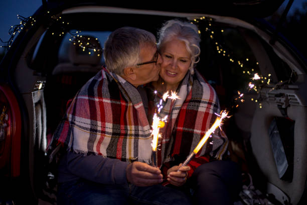 istock Senior couple sit in open car trunk and hold spark sticks in their hands 984973206