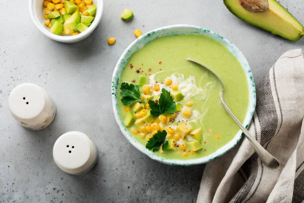 istock Homemade tender soup puree from avocado and corn with cream in rustic ceramic plate on gray concrete old background. Selective focus. Top view. Copy space. 984973396