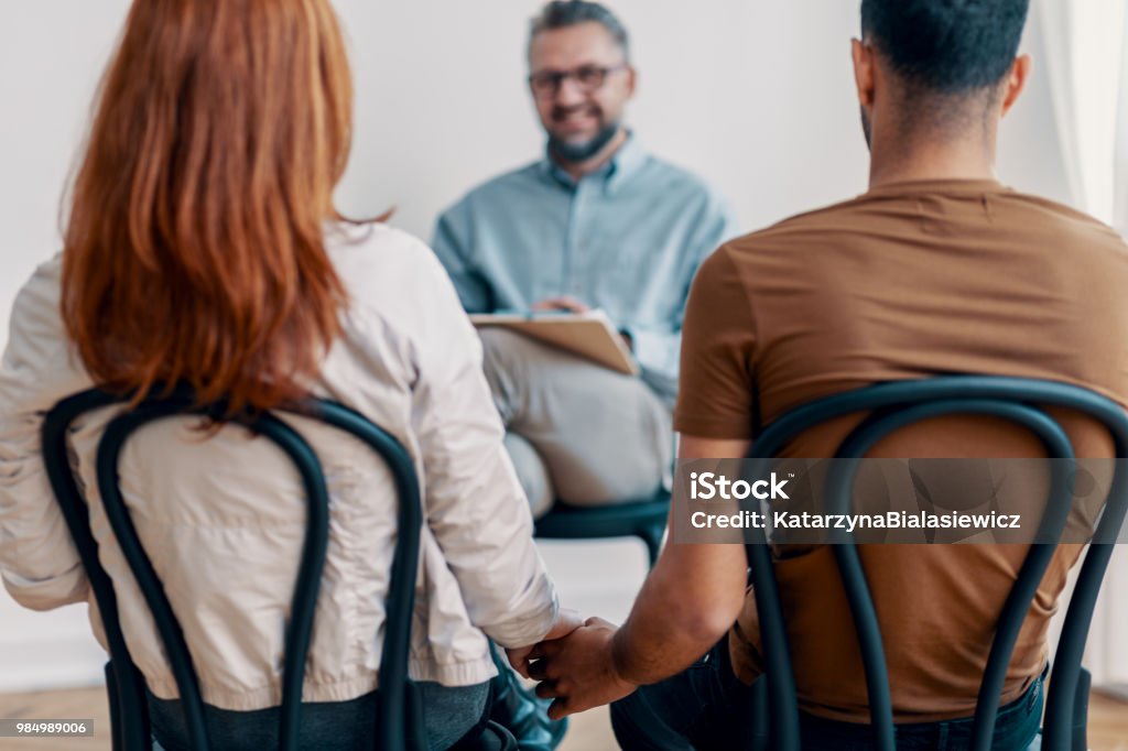 Giovane bella coppia che si tiene per mano durante l'incontro con il consulente - Foto stock royalty-free di Seduta di terapia