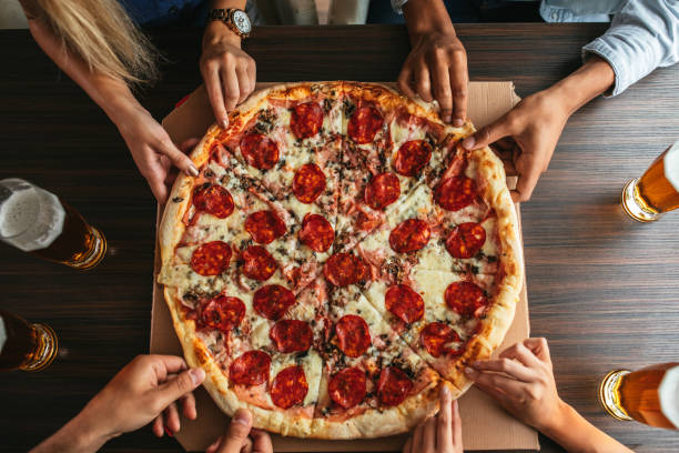 Dig in! High angle shot of a group of unrecognizable people's hands each grabbing a slice of pizza pizza stock pictures, royalty-free photos & images