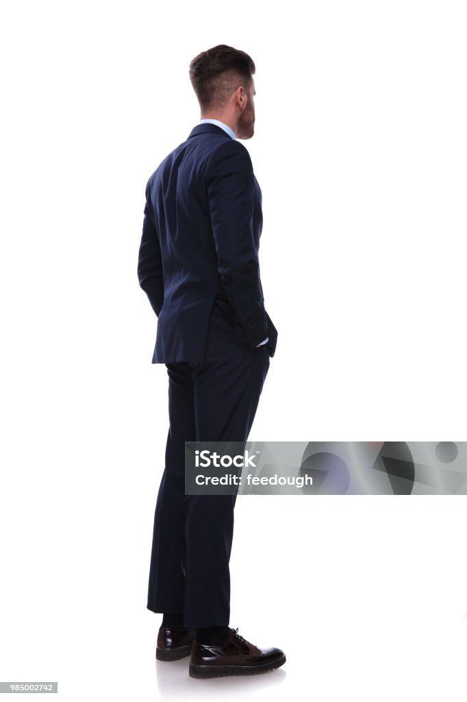 turned businessman in navy suit looks to side turned businessman in navy suit looks to side while standing on white background with hands in pockets Rear View Stock Photo