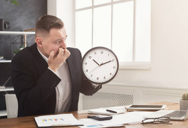 istock Worried businessman holding clock and looking at it 985006442