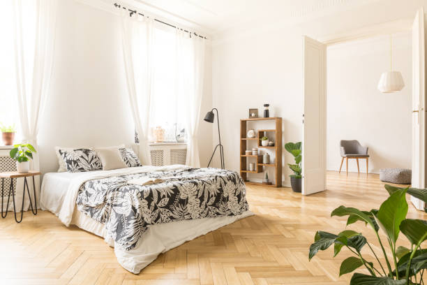istock Plant on table next to bed with patterned sheets in white bedroom interior with lamp. Real photo 985006630