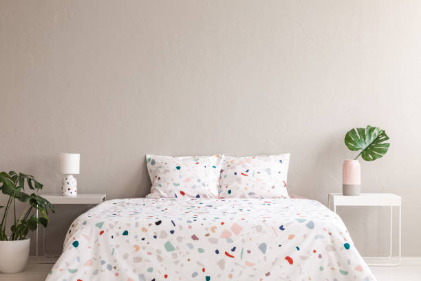 istock Patterned sheets on bed between tables with lamp and leaf in bedroom interior. Real photo 985012160