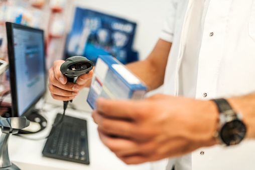 Photo of Caucasian pharmaceutical male worker scanning bar-code of medicine drug in a pharmacy drugstore with bar code reader.