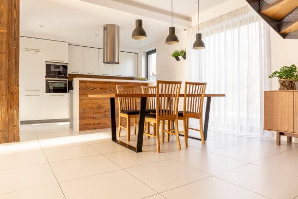 Spacious, open kitchen and dining room with wooden table and chairs, large window, white cupboards and tiles on the floor. Real photo Spacious, open kitchen and dining room with wooden table and chairs, large window, white cupboards and tiles on the floor. Real photo tiled floor stock pictures, royalty-free photos & images