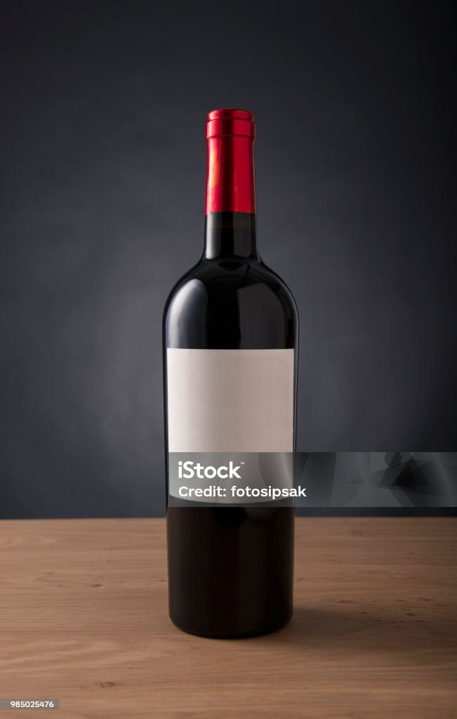 garrafa de vinho vermelha com rótulo em branco para qualquer marca no fundo preto aginst tabela - Foto de stock de Garrafa de Vinho - Garrafa royalty-free