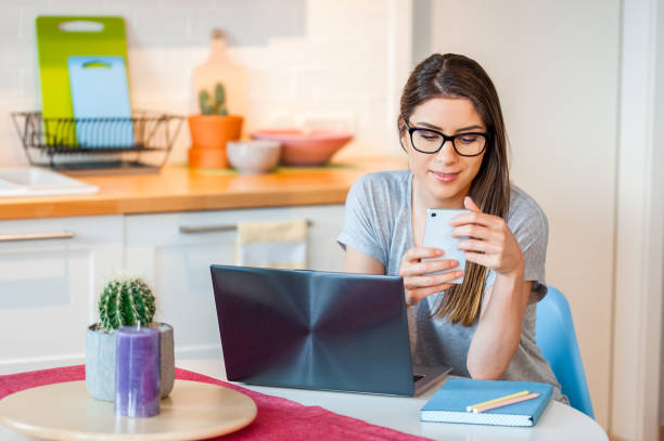 istock Girl at home sitting at table using laptop and phone 985034730