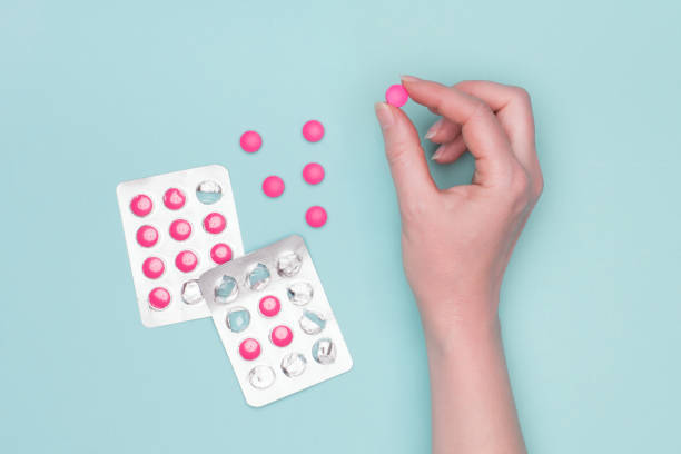 vista dall'alto della mano femminile che tiene la pillola da prescrizione rosa accanto alle confezioni blister su sfondo blu pastello. paziente malato che assume farmaci. - drug abuse narcotic medicine protection foto e immagini stock