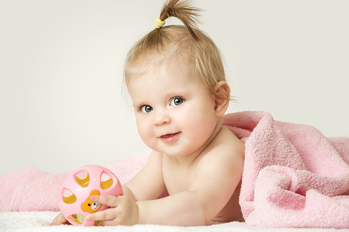 Studio portrait of adorable baby girl playing with plastic rattle toy