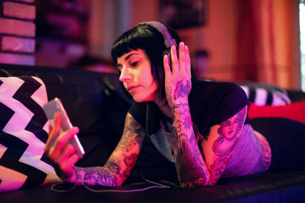 ソファでスマートフォンでリラックスしている若い女性 - headphones women tattoo music ストックフォトと画像