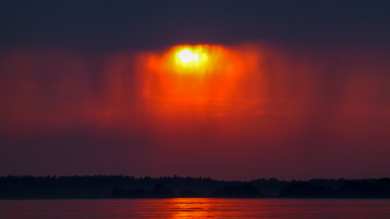Red sunset and dark rainy clouds reflected in calm water.