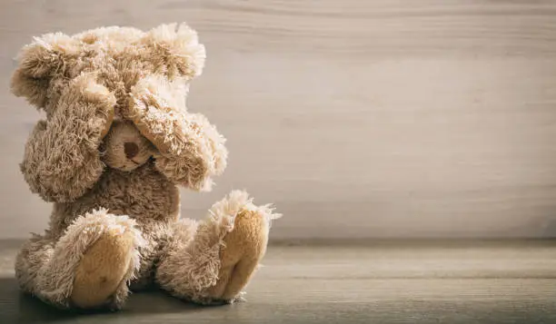 Child abuse concept. Teddy bear covering  eyes in an empty room