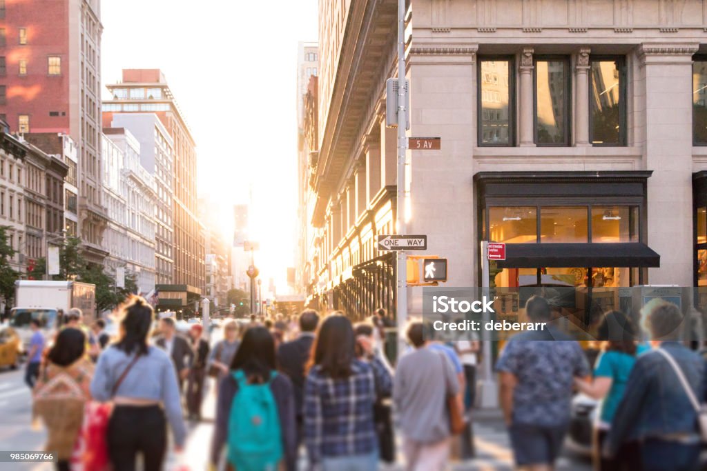 Un gruppo diversificato di persone anonime che camminano lungo la trafficata strada urbana con la luce del sole che brilla sullo sfondo a New York City - Foto stock royalty-free di New York - Città