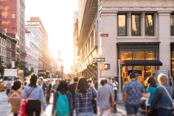 un gruppo diversificato di persone anonime che camminano lungo la trafficata strada urbana con la luce del sole che brilla sullo sfondo a new york city - dusk people manhattan new york city foto e immagini stock