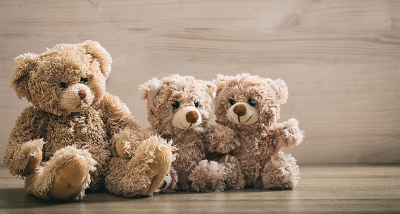 Parent and children teddy bears sitting on a wooden background