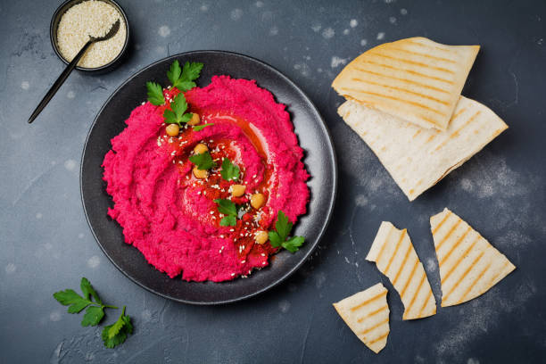 istock Homemade beetroot hummus in black ceramic dish on old dark concrete background. Selective focus. Top view. 985082624