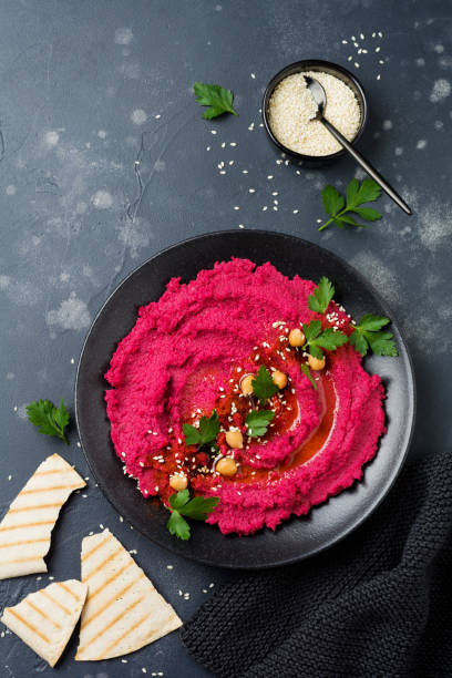 istock Homemade beetroot hummus in black ceramic dish on old dark concrete background. Selective focus. Top view. 985082672