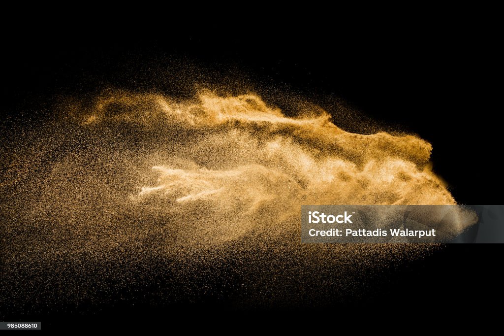 Golden colored sand splash against dark background. Yellow sand fly wave in the air. Gold - Metal Stock Photo