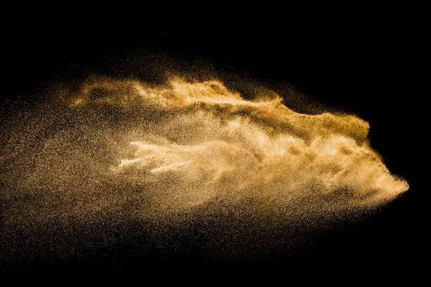 Photo of Golden colored sand splash against dark background. Yellow sand fly wave in the air.