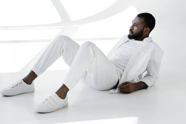 istock handsome stylish african american man in white clothes lying on white 985091394