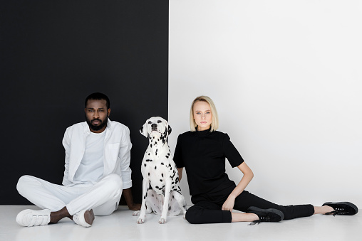 multicultural couple sitting near black and white wall with dalmatian dog