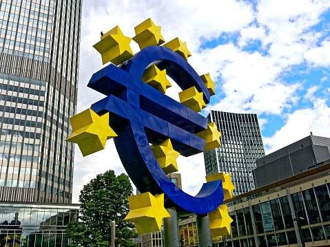 Frankfurt, Germany: The blue Euro-Sign with yellow stars in front of skyscrapers with dramatic sky.
