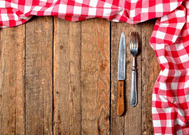 istock Red checkered tablecloth top and right frame, knife and fork on vintage wooden table background - view from above 985103248