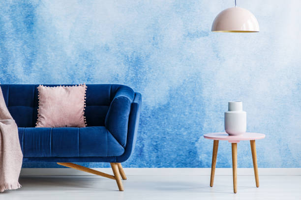 istock Blue and soft pink minimal style living room. Interior with dark couch, small side table and hanging lamp against ombre background. Real photo. 985113948