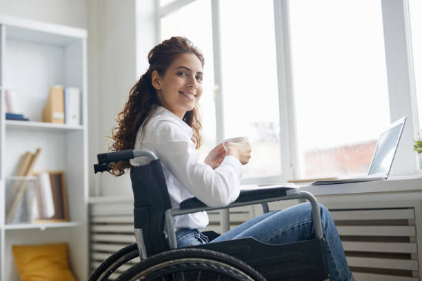 Office manager Young smiling manager with cup of tea looking at you while sitting by office window wheelchair photos stock pictures, royalty-free photos & images