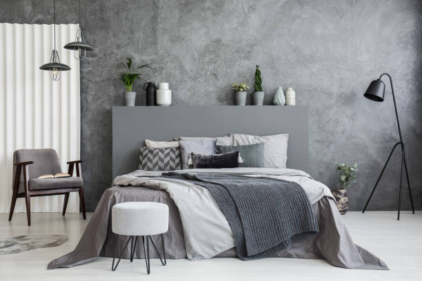 Grey stool in front of bed with blankets and cushions in dark hotel bedroom interior. Real photo stock photo