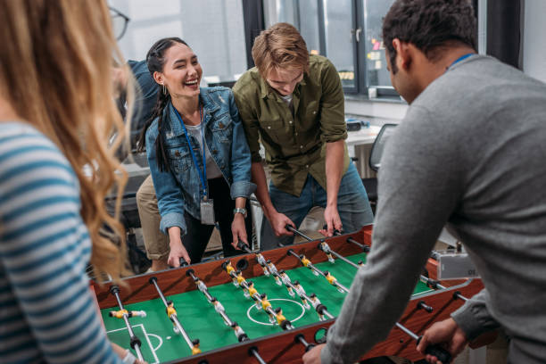 persone multiculturali felici che giocano a calcio da tavolo in ufficio moderno - biliardino foto e immagini stock