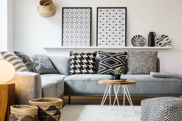 istock Patterned pillows on grey corner sofa in apartment interior with posters and pouf. Real photo 985128552