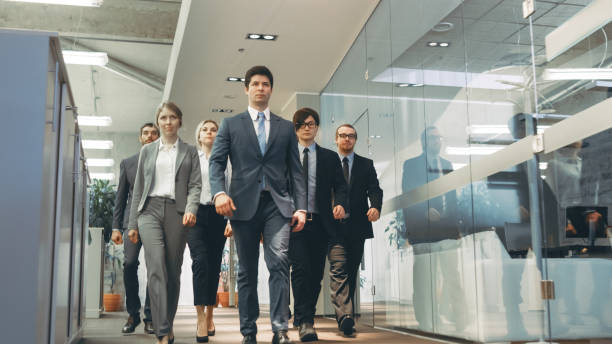 diverso equipo de delegados / abogados marchando con confianza a través de la empresa edificio de pasillo. multicultural multitud de empresarios decididos en oficinas de vidrio y mármol con estilo. - global politics fotografías e imágenes de stock