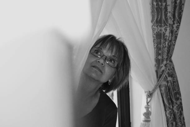 istock Woman Looking Through Curtain At Home 985130132