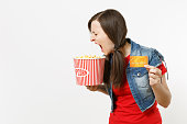 Portrait of young crazy loony brunette woman in casual clothes watching movie film, holding bucket of popcorn and credit card, screaming isolated on white background. Emotions in cinema concept.