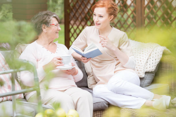 istock Caregiver reading book while senior woman drinking tea on the terrace 985147070