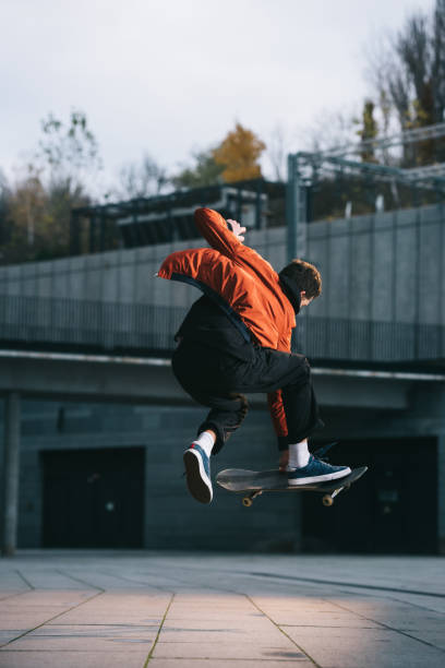 istock skateboarder in red jacket performing jump trick in urban location 985158532