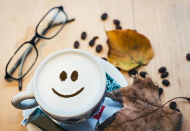Coffee cup and coffee beans on wooden table. Sign in foam represents smiley face.