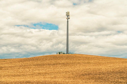 Mobile phone base station in the middle of ripe wheat field in Toscana landscaped against cloudy sky in beginning of summer.