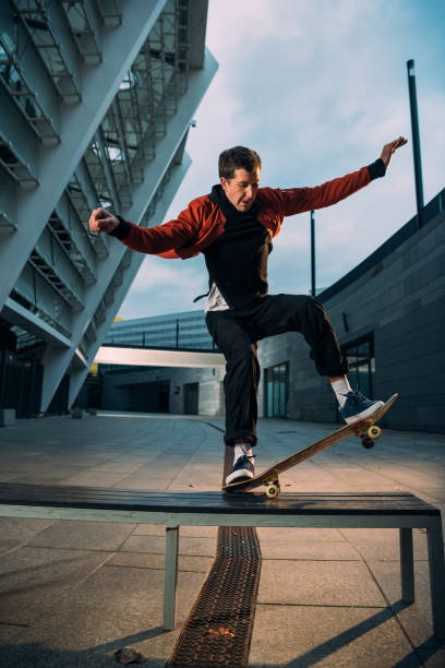 istock young skateboarder in stylish outfit balancing with board on bench 985162832