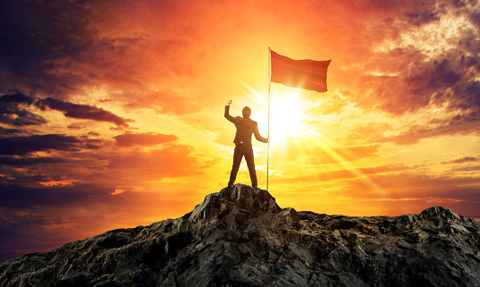 Businessman with flag on mountain top. Concept for success.