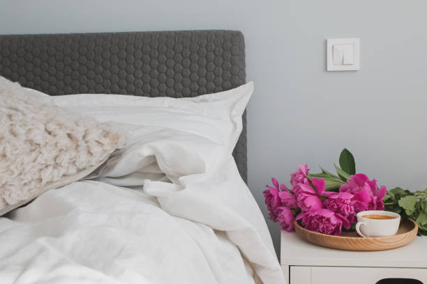 istock Bed with white bed sheets and pink peonies and coffee on the nightstand. 985186952
