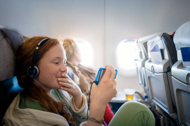 ragazza su un aereo che guarda un film su un telefono cellulare - airplane smart phone travel mobile phone foto e immagini stock