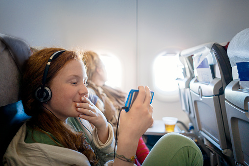 Girl sitting in an airplane passing time on her mobile phone watching a movie while waiting for landing