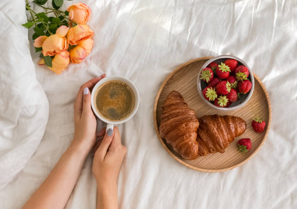 istock Woman's hands holding a cup of coffee on the bed with white bedsheet. 985188534