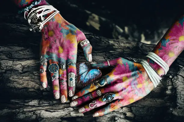 closeup of woman colorful hands with lot of rings on tree surface in heart shape  with butterfly in the middle composite photo