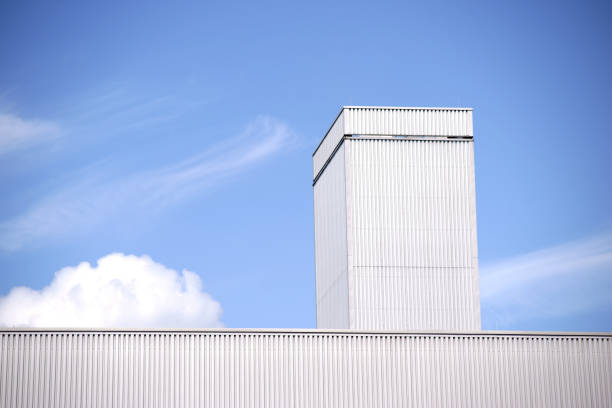 The roof edge of an industrial hall made of corrugated iron in front of a blue sky with clouds.