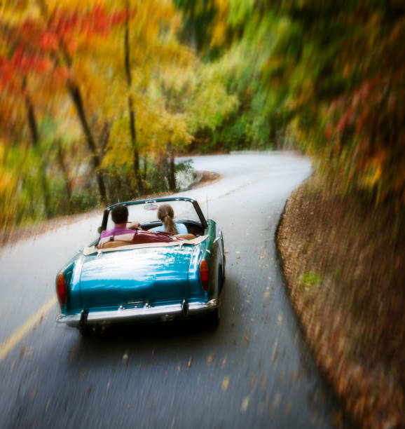 Couple driving down road in the mountains with colorful fall trees.